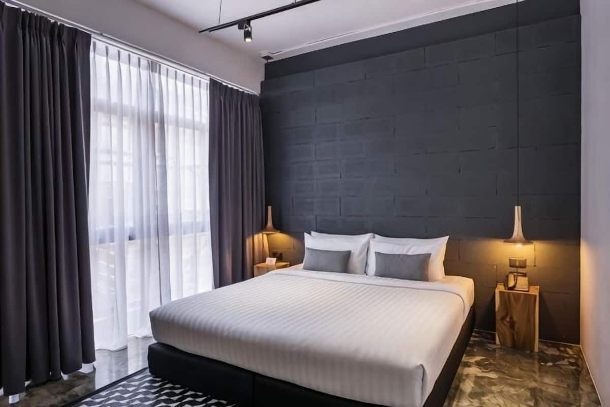 A modern bedroom with a large bed, dark wall paneling, and two bedside lamps.