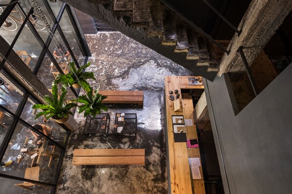 Una habitación espaciosa con techos altos, una ventana grande, un banco de madera, una mesa pequeña y una planta en maceta.
