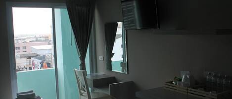 A hotel room with a bed, a desk, a chair, a TV, and a view of the city through a large window.