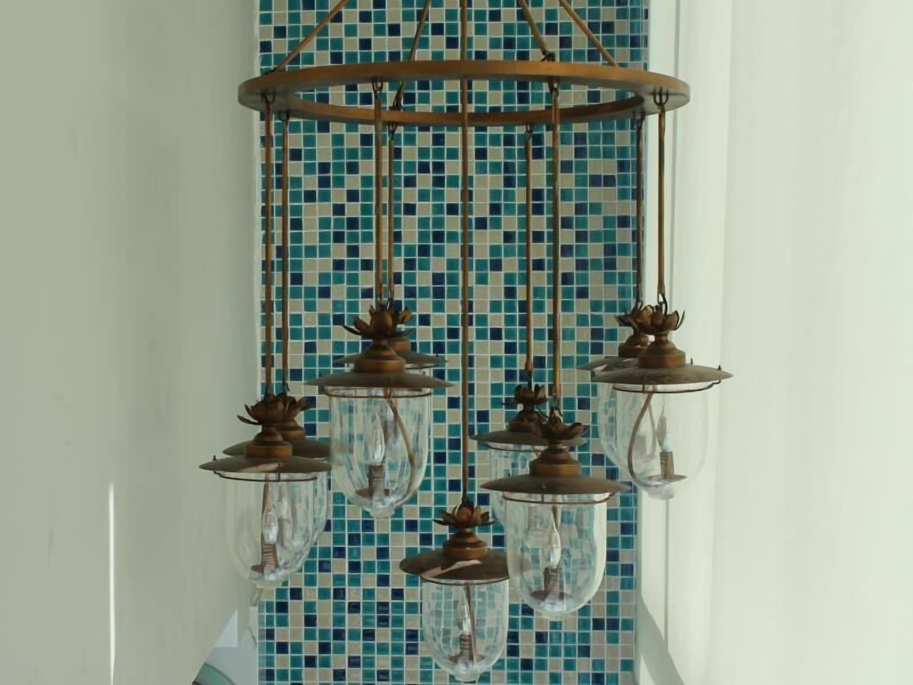 A chandelier with multiple glass shades and metal fixtures against a tiled wall.