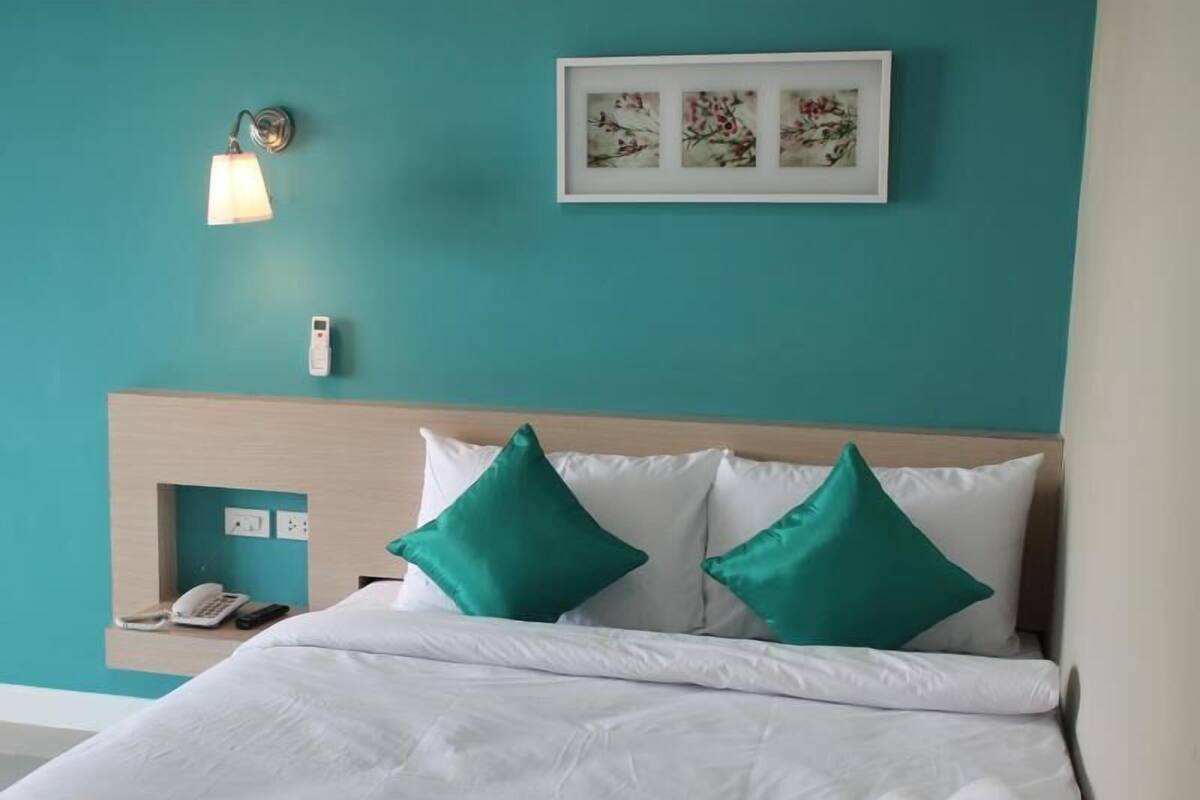 Habitación de hotel con paredes verde azuladas, cabecera de madera, ropa de cama blanca y dos almohadas verdes.