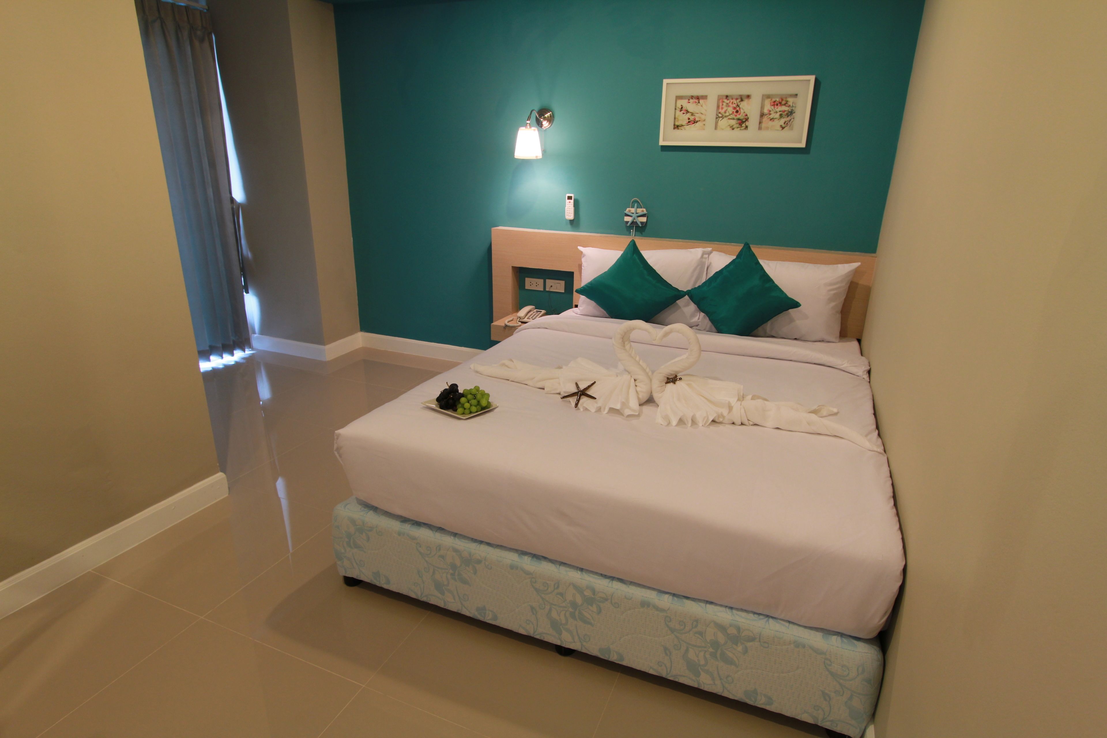 A hotel room with a large bed, teal walls, a nightstand with a phone, and a wall-mounted light.