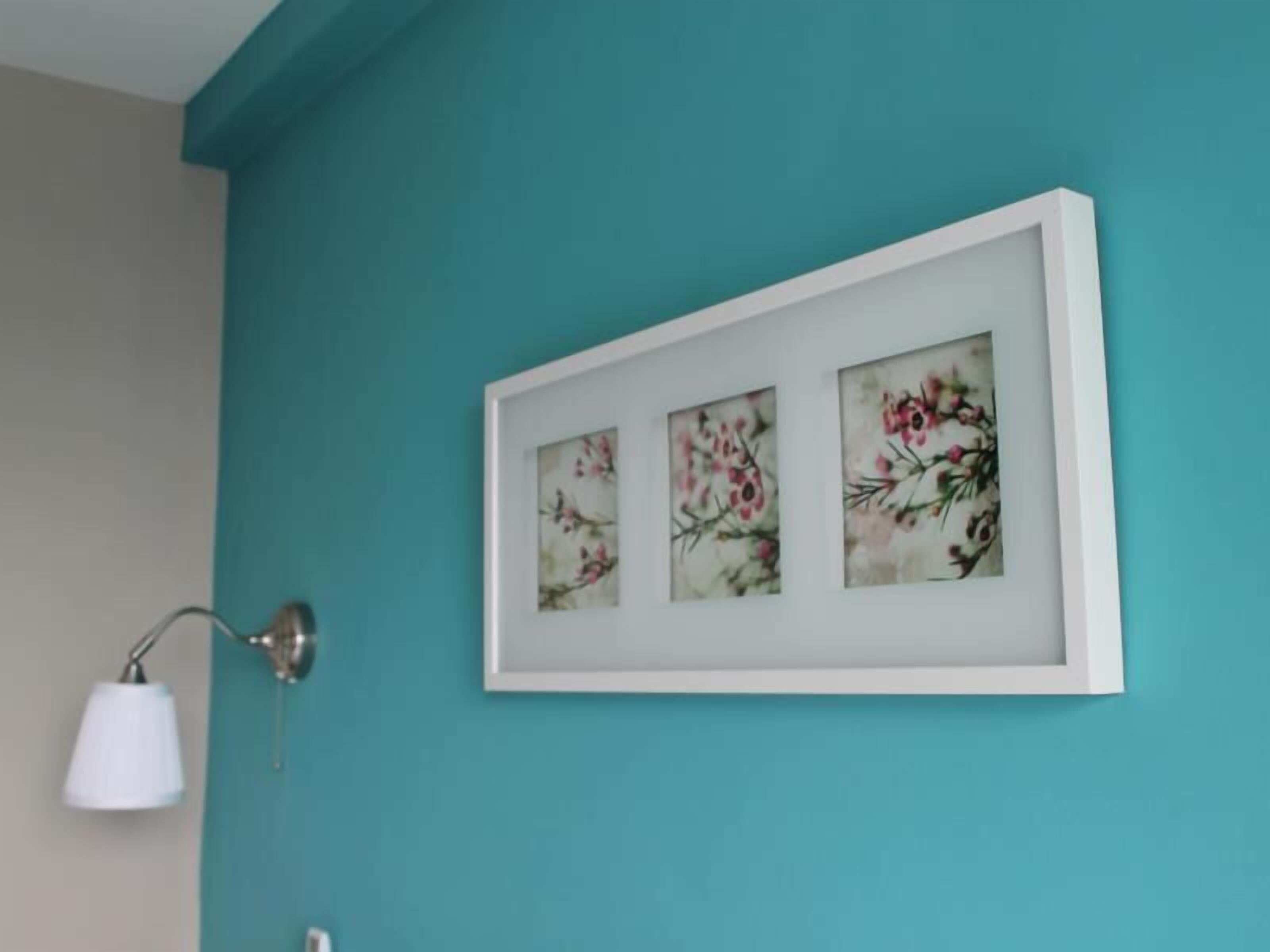 A teal wall with three framed floral artworks.