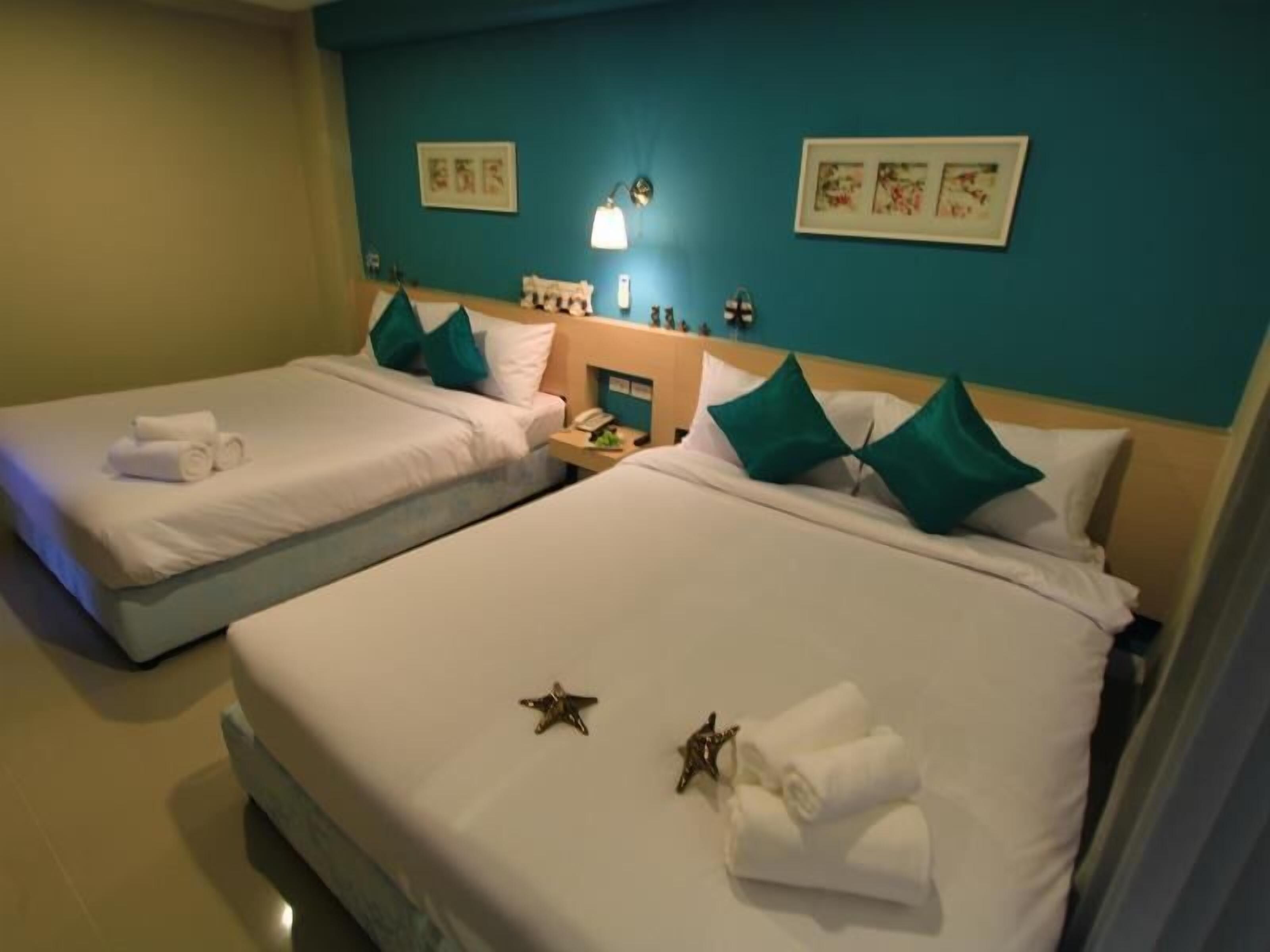 Quarto de hotel com duas camas, paredes verde-água e obras de arte.