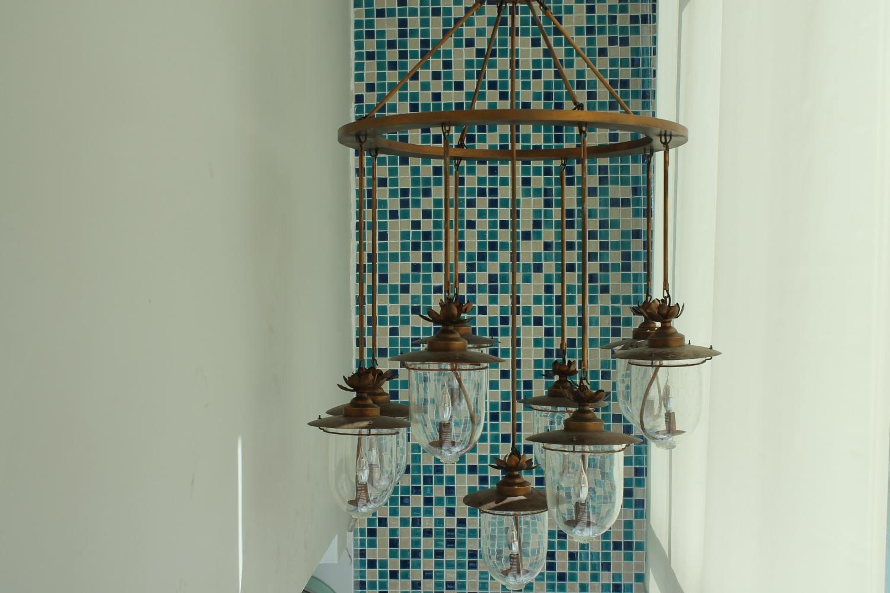 Um candelabro com várias esferas de vidro e detalhes metálicos, em frente a uma parede revestida com azulejos.