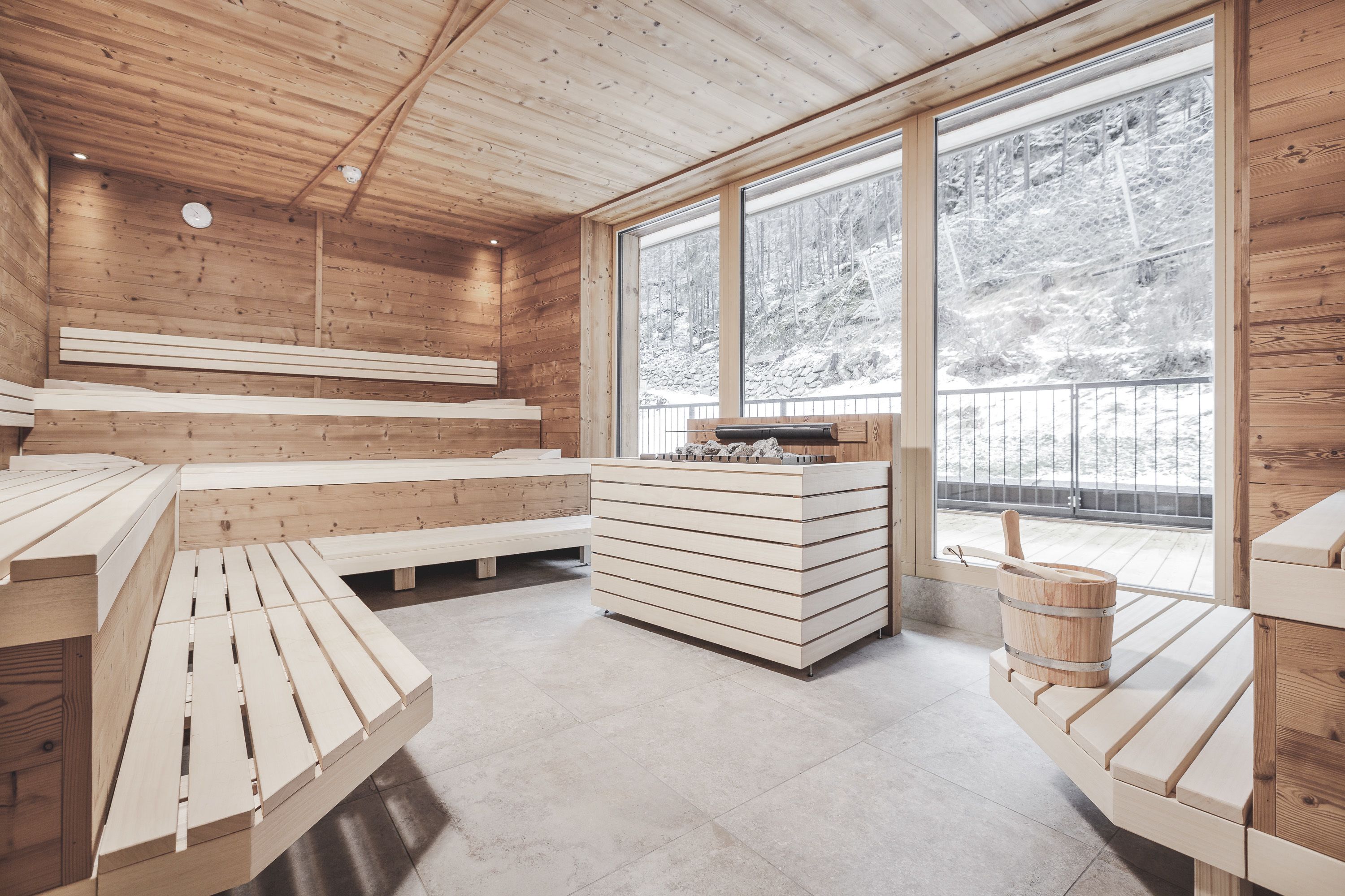A wooden cabin interior with a bench seating area, a wooden table, and a large window offering a view of a snowy landscape.