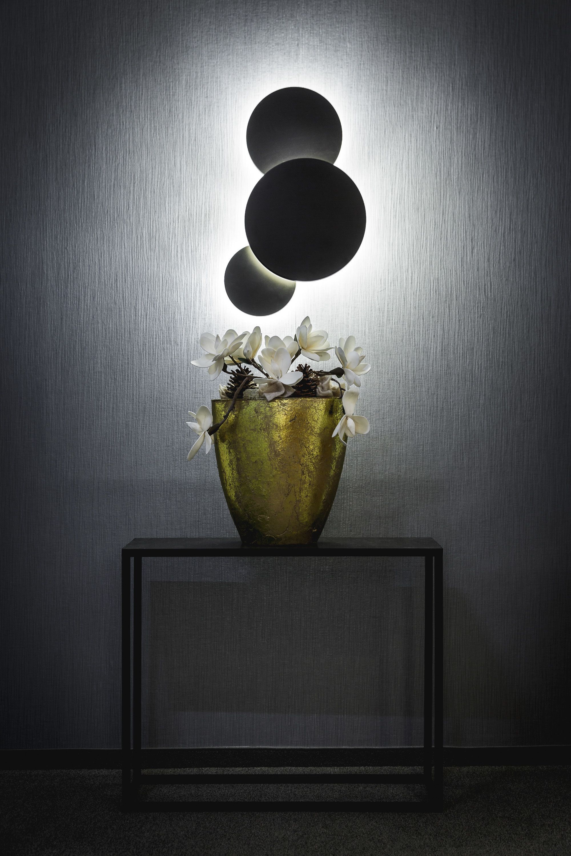 A gold vase with white flowers on a black console table against a textured wall.