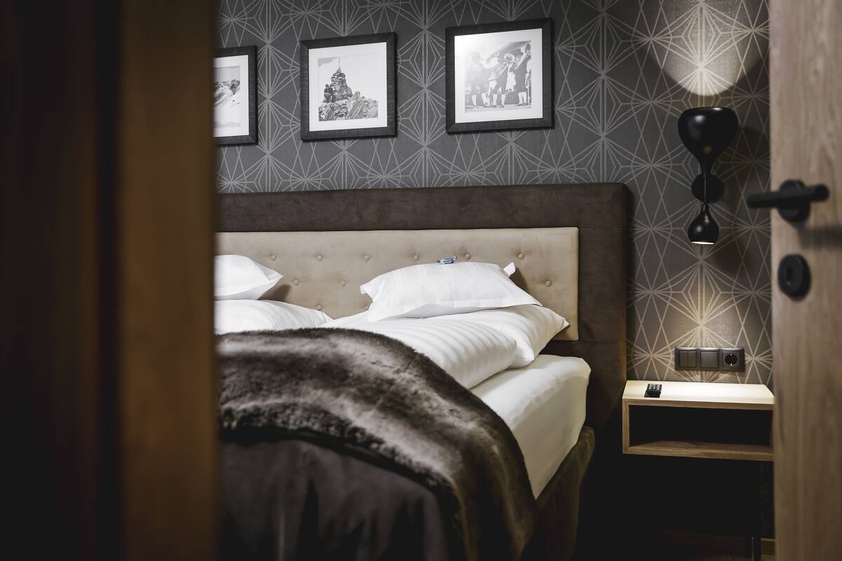 Un dormitorio con cabecera capitonada, una mesita de noche con lámpara y cuadros en la pared.