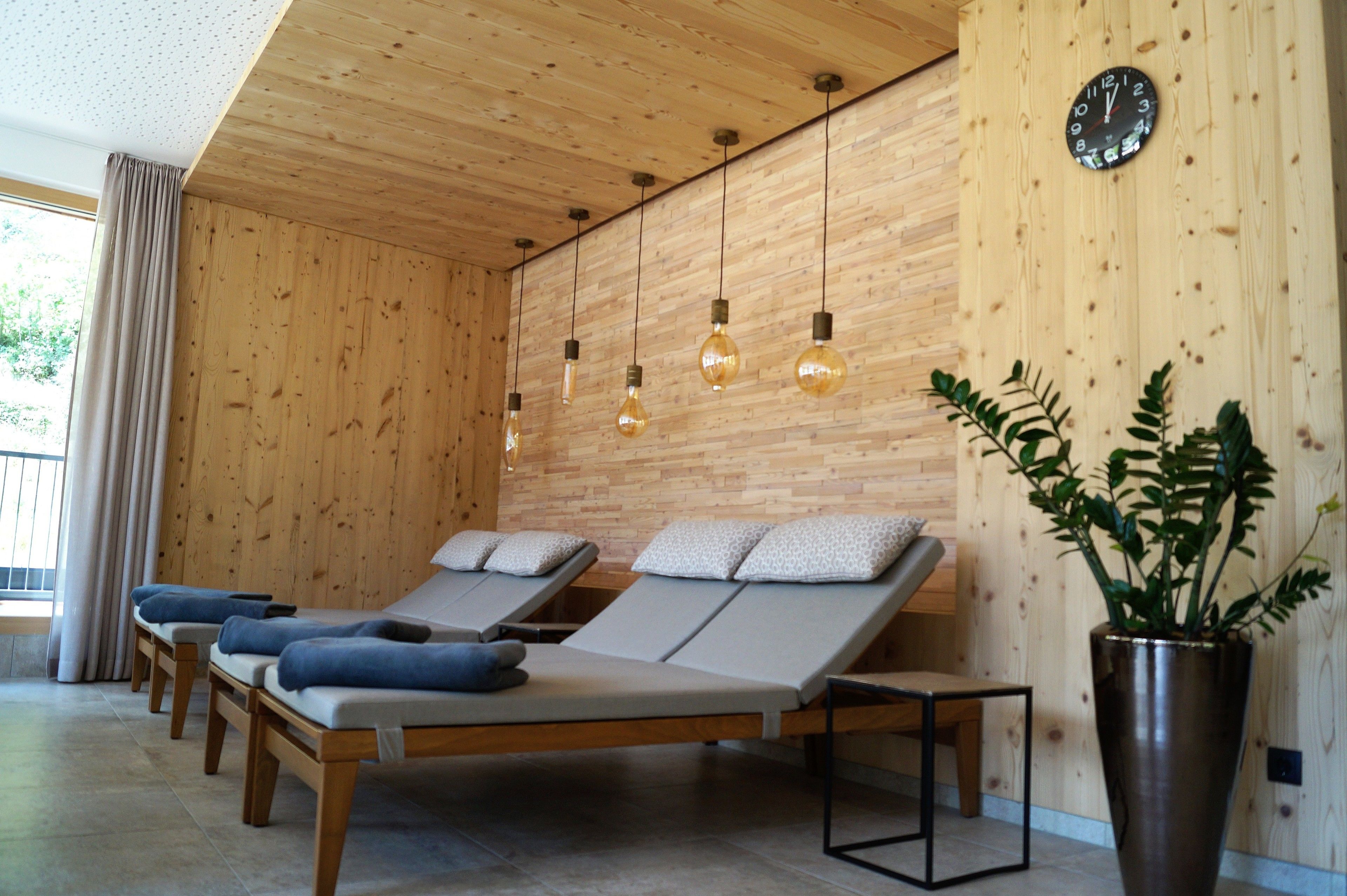 A room with wooden walls, a clock, and four lounge chairs with cushions.