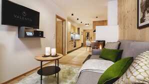 Un salon moderne avec un canapé gris, des coussins verts, une petite table ronde avec des bougies et un téléviseur à écran plat fixé au mur.