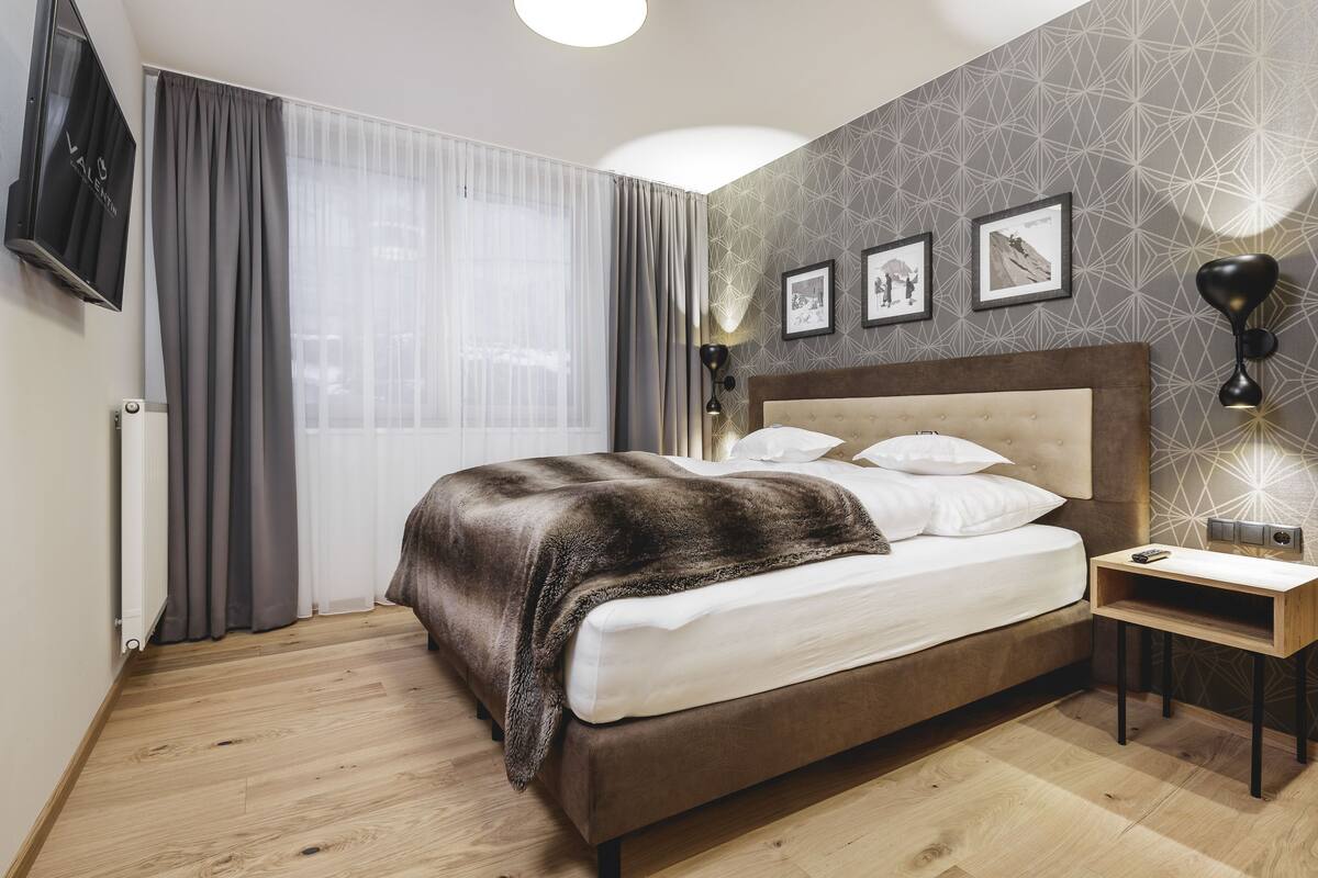 Un dormitorio moderno con una cama grande, una mesita de noche, un televisor y una lámpara de pared.