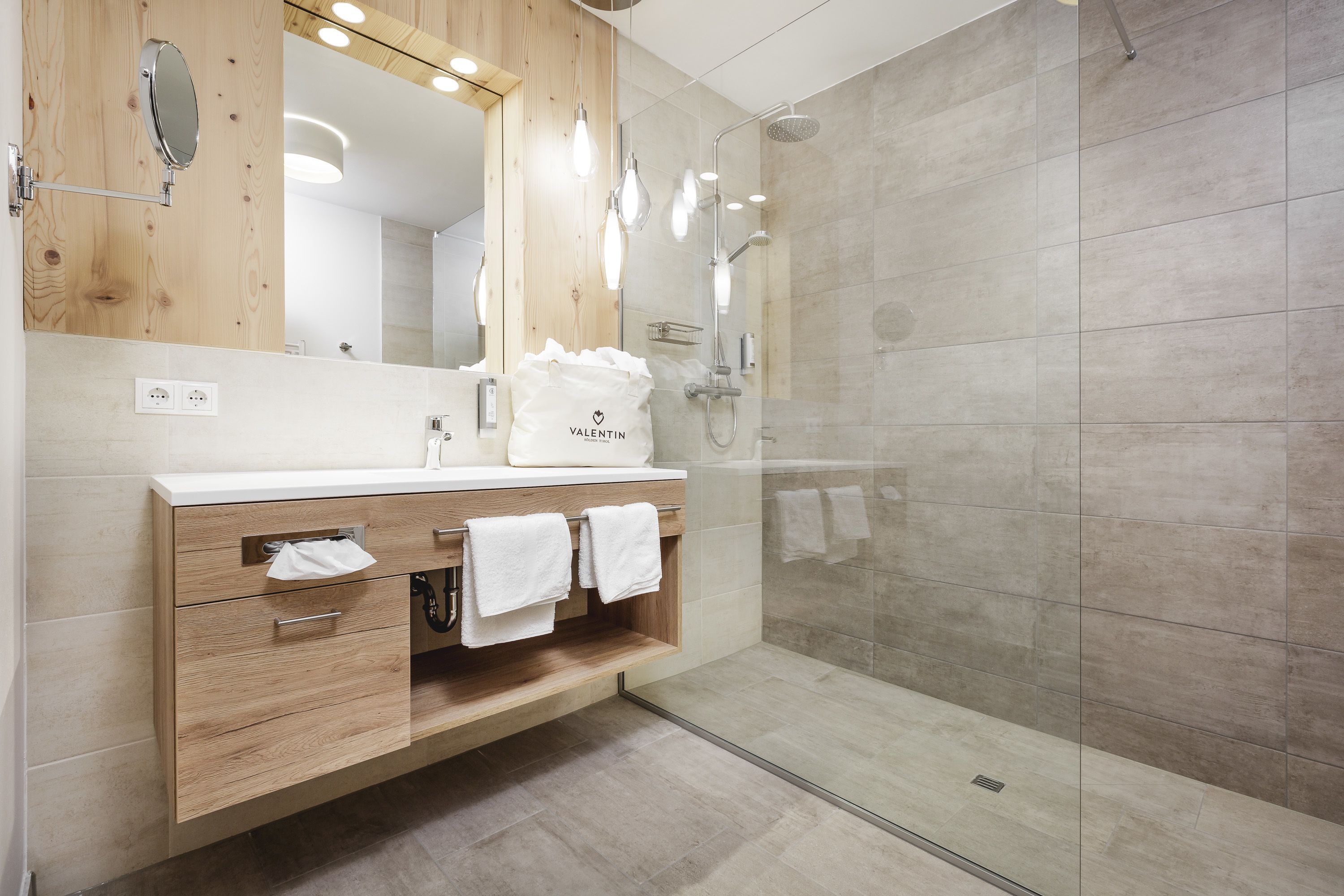 Un baño moderno con tocador de madera, un espejo grande y zona de ducha con mampara de cristal.