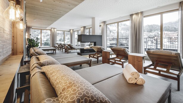 Un salon moderne doté d’un plancher en bois, de grandes fenêtres offrant une vue sur un paysage enneigé et d’un téléviseur à écran plat fixé au mur.