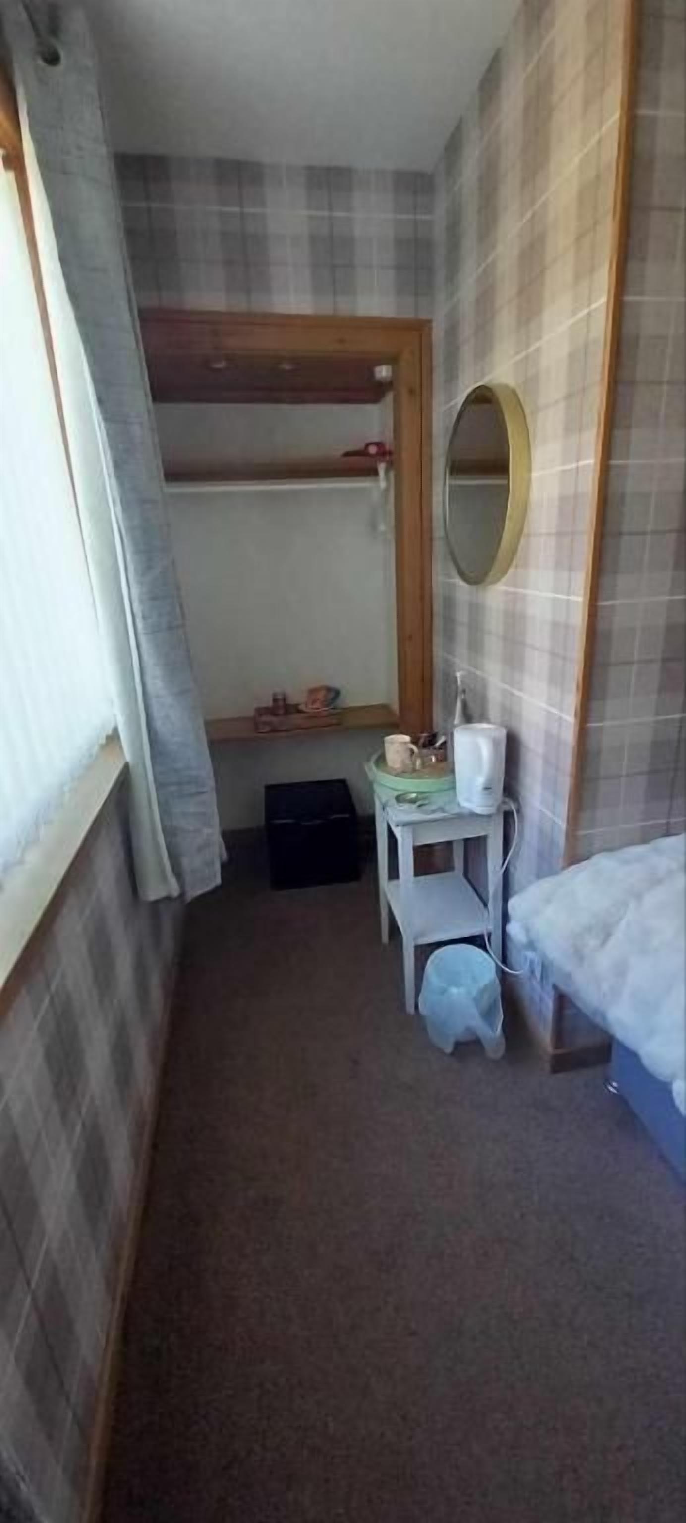 A narrow room with a bunk bed, a small table with a mirror, and a white sink.