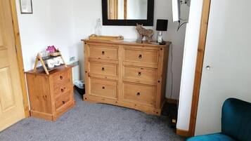 A room with a wooden dresser, a mirror, a blue chair, and a small shelf with items.