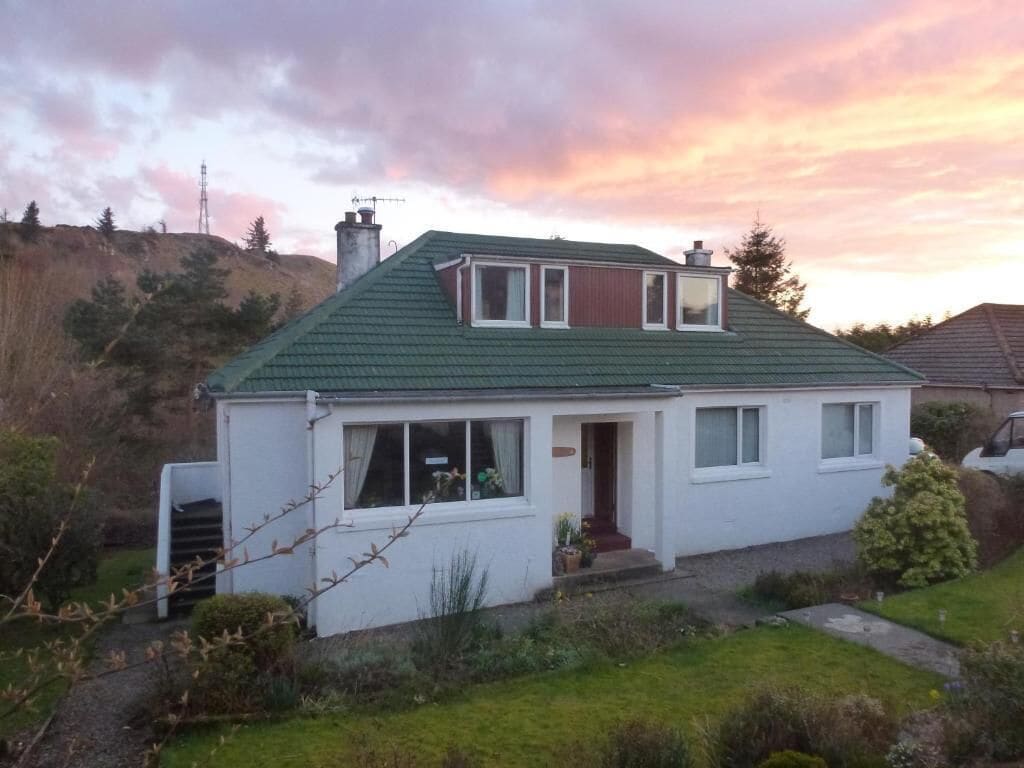 A two-story house with a green roof, white exterior walls, and a small front porch.