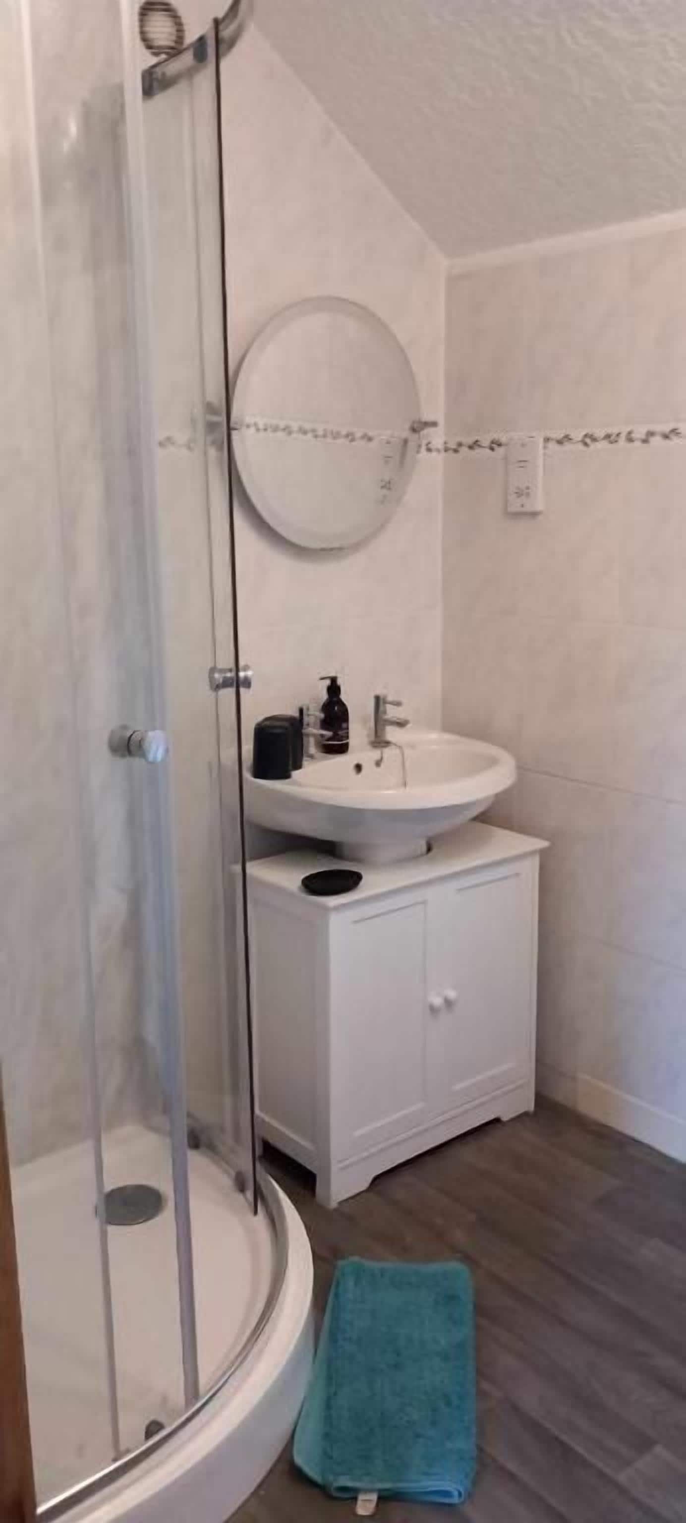 A bathroom with a glass-enclosed shower, a round mirror, a sink, and a cabinet.