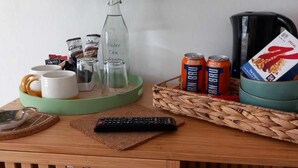 A wooden table with a remote control, a glass bottle, a mug, a tray with cans, and a coffee maker. - Don Muir Guest House (Oban)