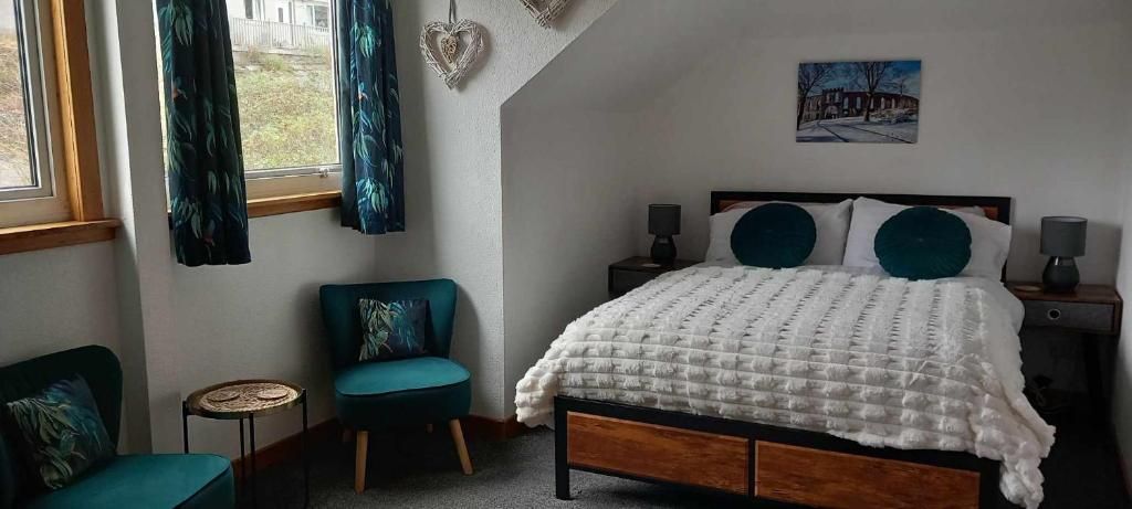 A bedroom with a bed, a chair, a small table, and a window with curtains.