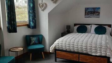 A bedroom with a bed, a chair, a small table, and a window with curtains.