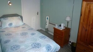 Un dormitorio con una cama, un aparador de madera, una mesita de noche, una lámpara y un televisor montado en la pared.