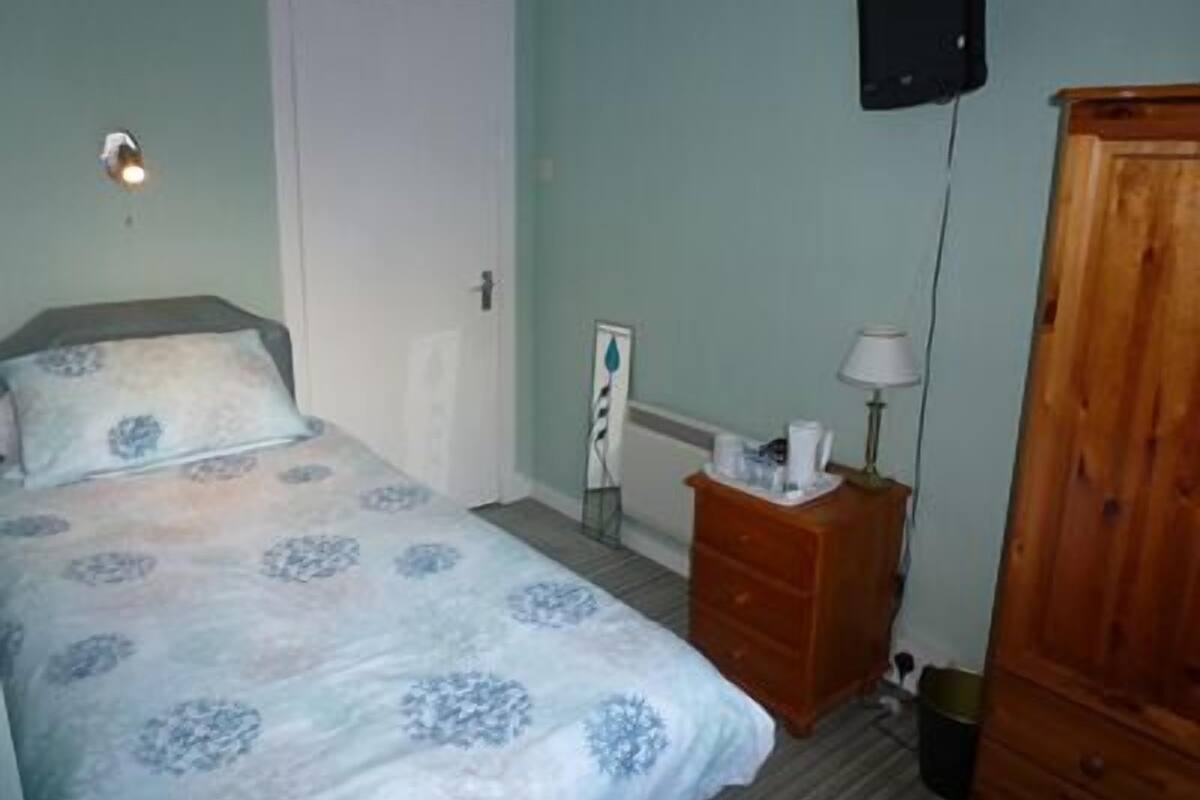 A bedroom with a bed, a wooden dresser, a nightstand, a lamp, and a TV mounted on the wall.