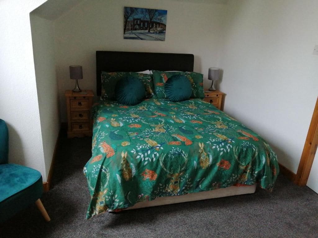 Een slaapkamer met een bed, twee nachtkastjes, een fauteuil en een schilderij aan de muur.