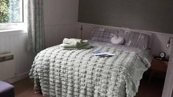 A bedroom with a bed, a chair, a window, and a radiator.
