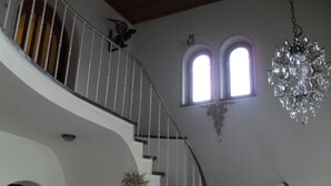 A grand staircase with a curved design, leading to an upper floor. There are two arched windows on the wall, and a chandelier hangs from the ceiling. - Hotel Garni Forsthaus (Ruhpolding)