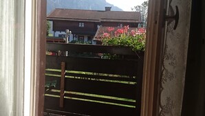 A wooden deck with a view of mountains and a house in the background. - Hotel Garni Forsthaus (Ruhpolding)