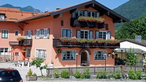 A traditional chalet with a balcony adorned with flowers, a wooden fence, and a mountain backdrop. - Hotel Garni Forsthaus (Ruhpolding)