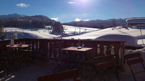 A snow-covered landscape with a clear sky, a ski lift, and a wooden outdoor seating area with tables and chairs. - Hotel Garni Forsthaus (Ruhpolding)