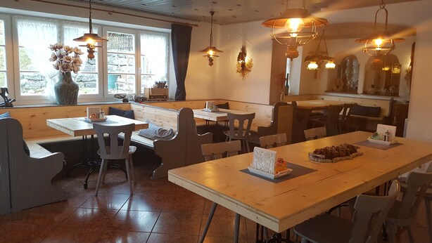 A cozy restaurant with wooden tables and benches, pendant lighting, and a large window with a view of the outdoors. - Hotel Garni Forsthaus (Ruhpolding)