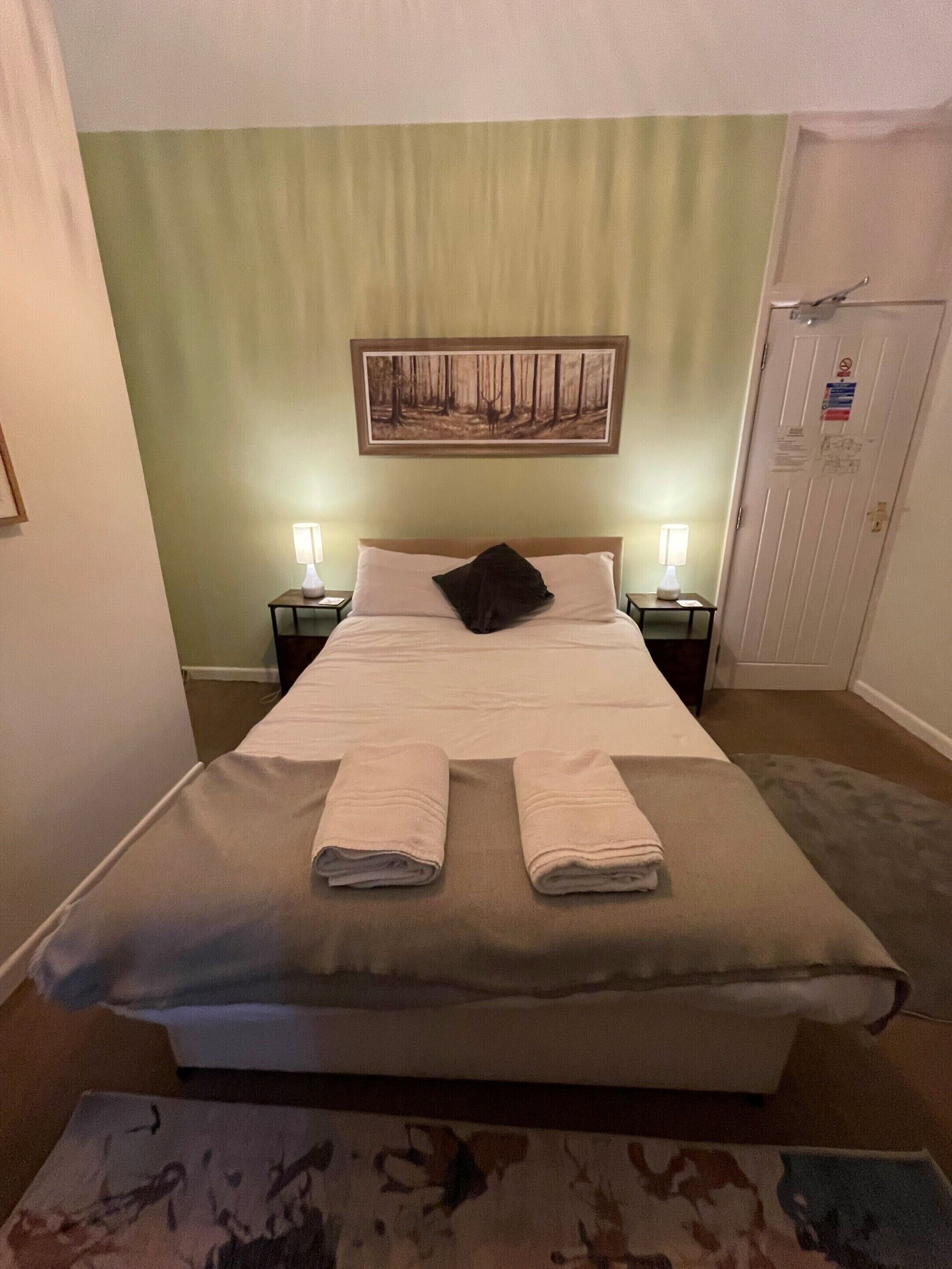 A hotel room with a bed, two bedside tables with lamps, a painting on the wall, and a door with a sign.