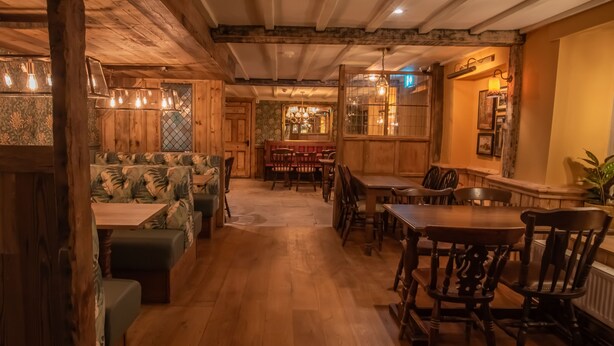 Un interior acogedor y rústico con vigas de madera, una zona de bar y diferentes disposiciones de asientos.