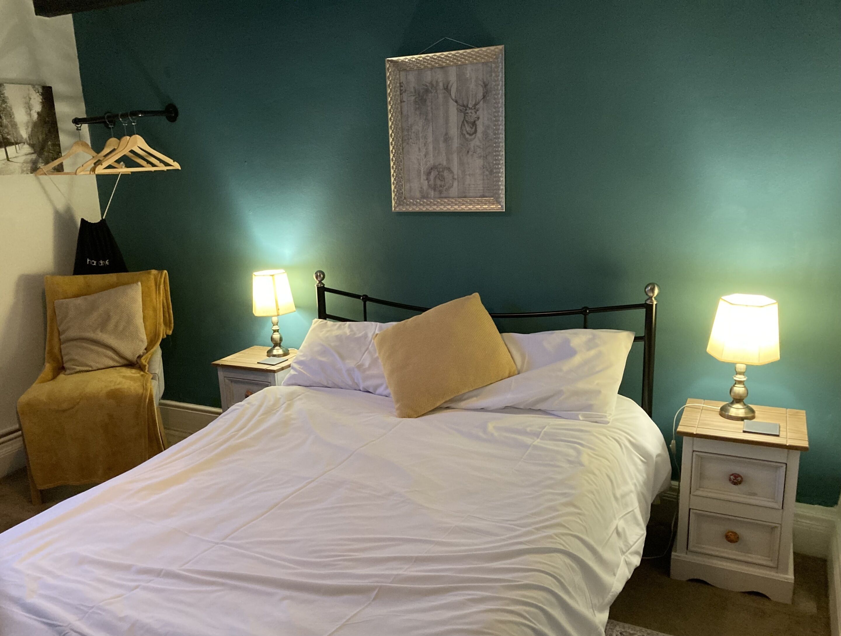 A neatly made bed with white linens, two bedside tables with lamps, a wooden chair, and a wall-mounted picture.