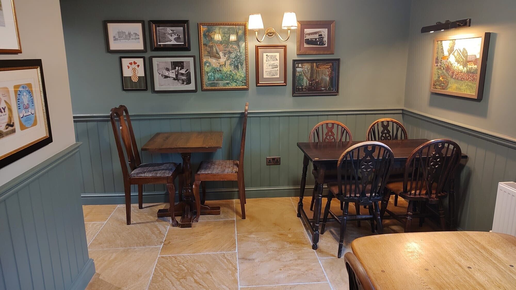 A dining area with a wooden table and chairs, framed pictures on the wall, and a light fixture above the table.