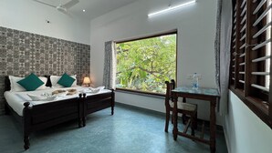 Un dormitorio con cama, escritorio, silla, ventilador de techo y ventana con vista a vegetación.