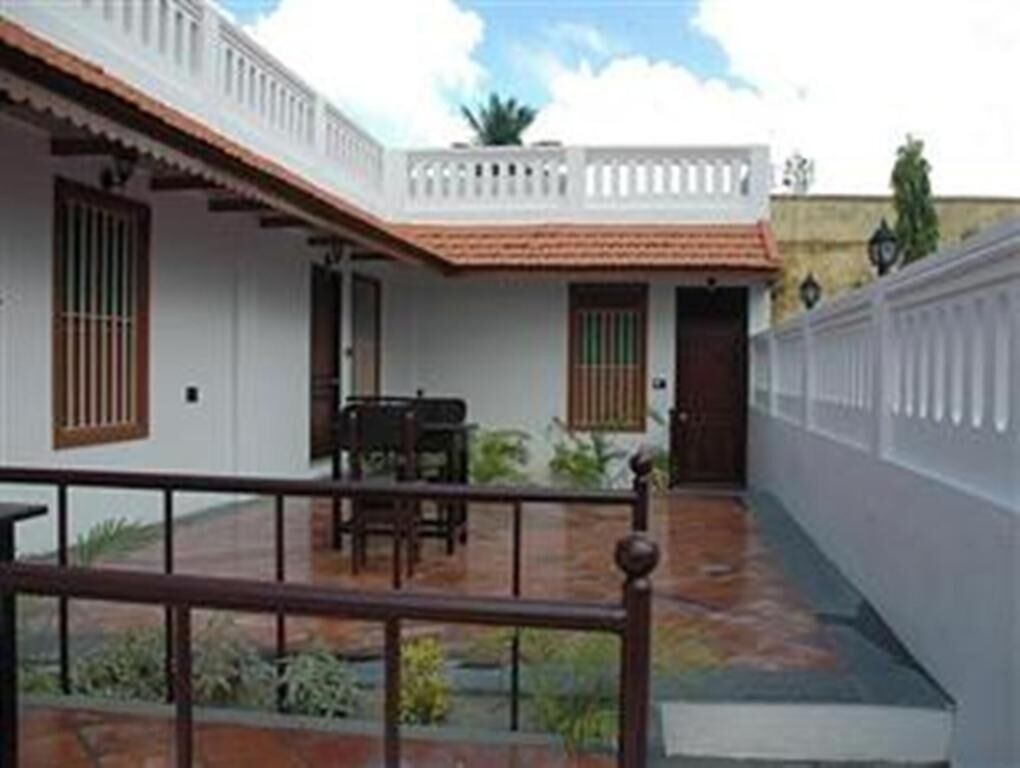 A two-story house with a balcony, a patio with a table and chairs, and a small garden area.