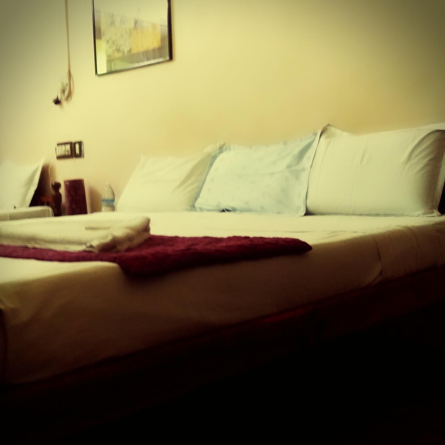 Una cama con almohadas blancas y azul claro, una colcha roja y una mesita de noche de madera con una lámpara.