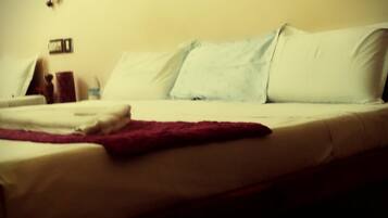 Una cama con almohadas blancas y azul claro, una colcha roja y una mesita de noche de madera con una lámpara.