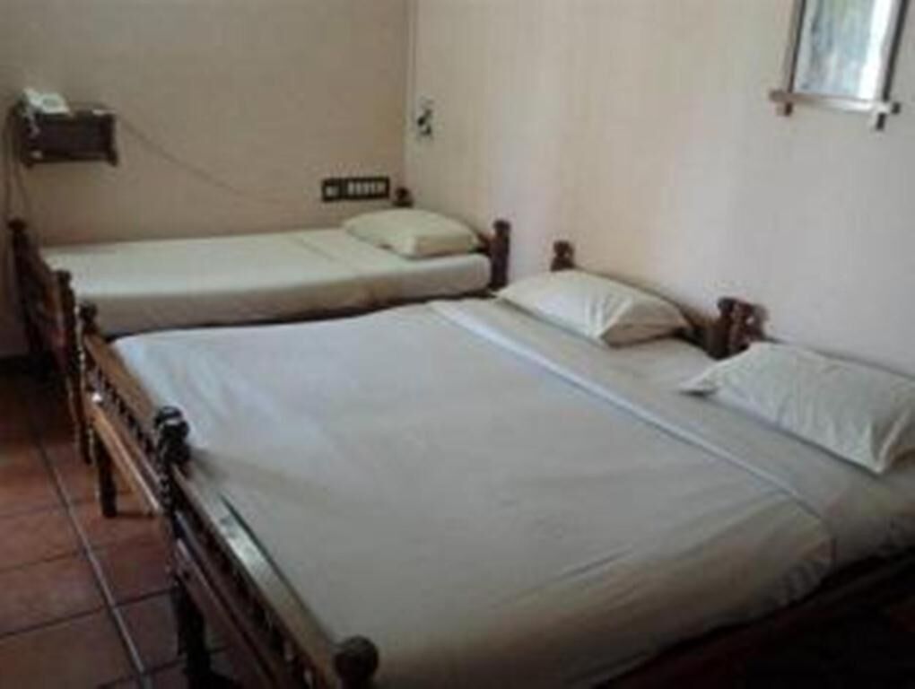 A room with two single beds, a small bedside table, and a wall-mounted shelf.