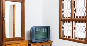 A room with a wooden cabinet, a television on a small wooden stand, and a window with a wooden lattice design. - Hotel Coramandal Heritage (Puducherry)