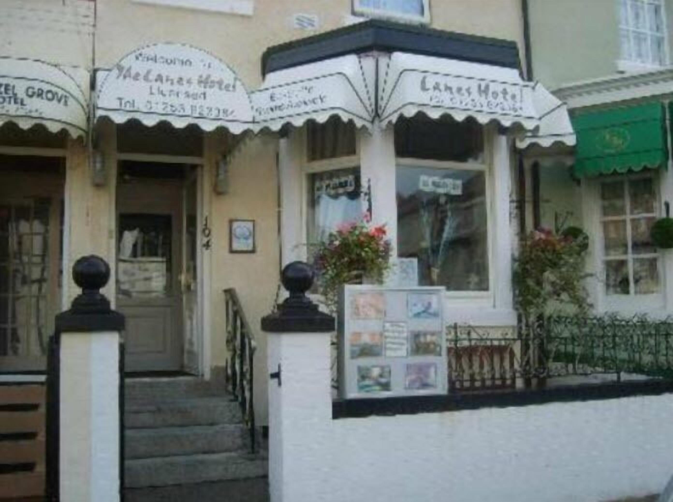 A building with a sign for 'Yealanth Hotel' and 'Lakes Hotel'. There are steps leading to the entrance, a small garden with flowers, and a green awning on one side.