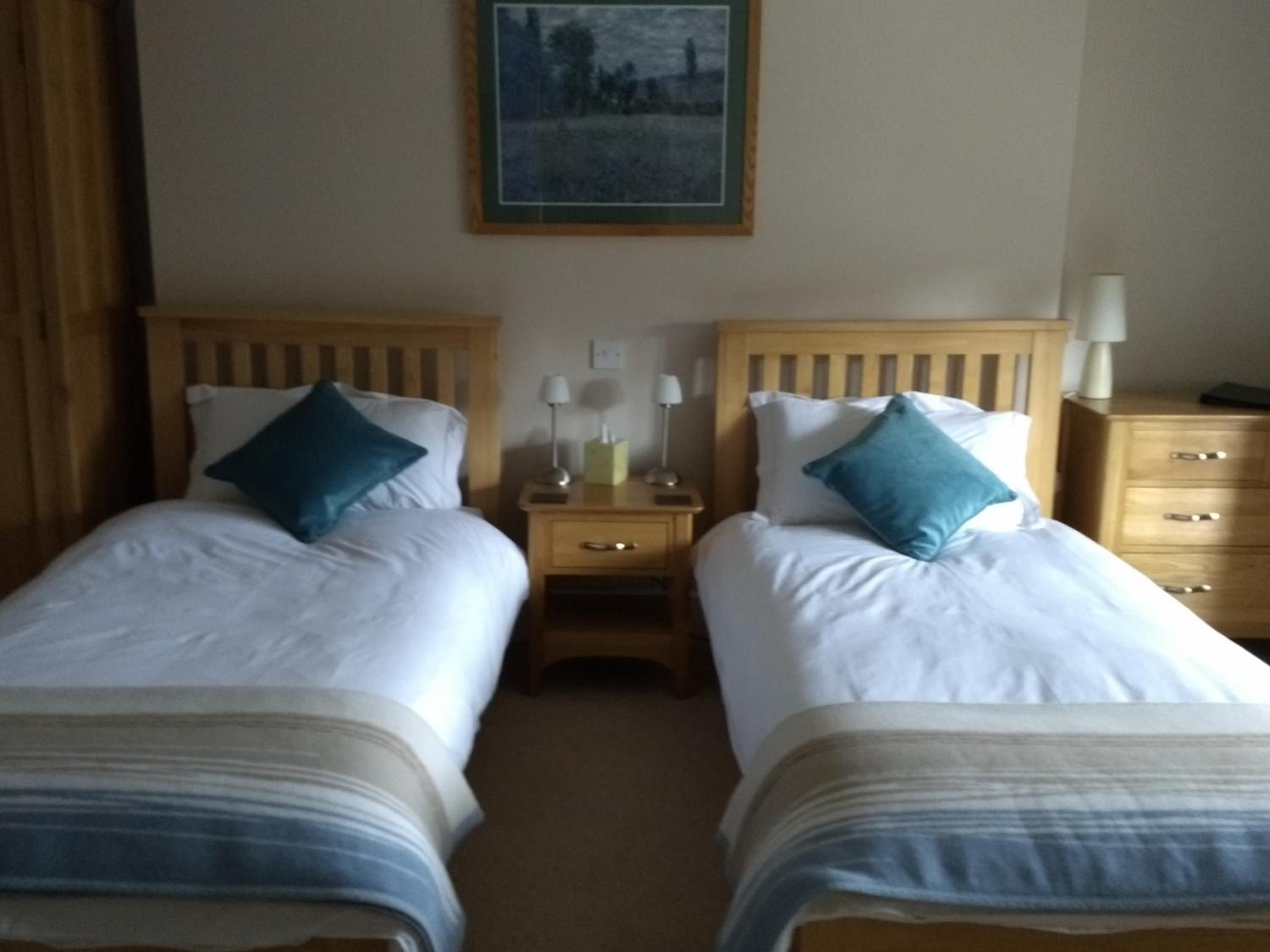 A hotel room with two single beds, each with a pillow and a bedside table with a lamp.