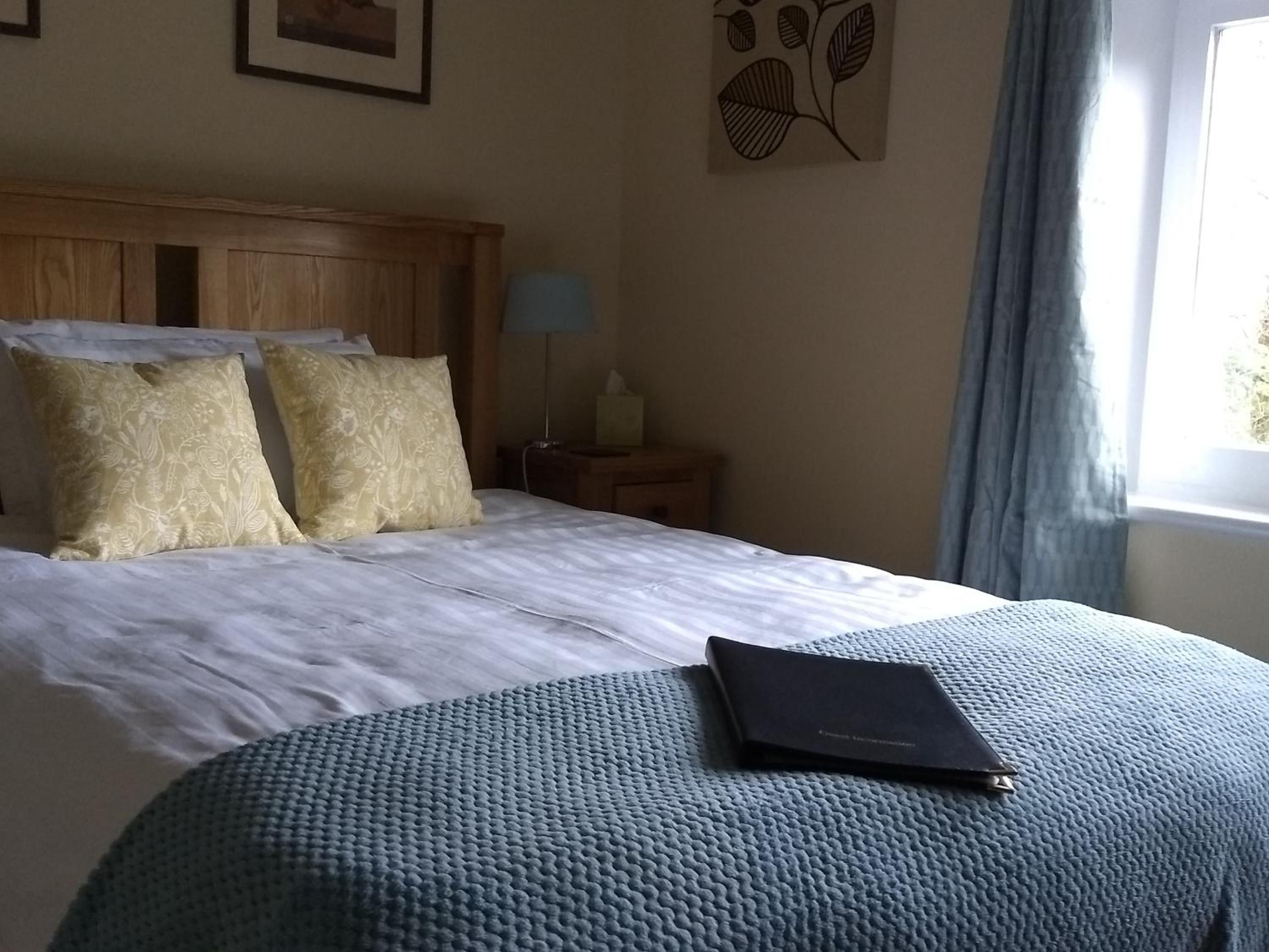 Hotellihuone, jossa on sänky, tyynyjä, yöpöytä lampun kanssa ja ikkuna, jossa on verhot.