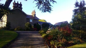 A gravel driveway leading to a house with a chimney, surrounded by well-maintained gardens and trees.