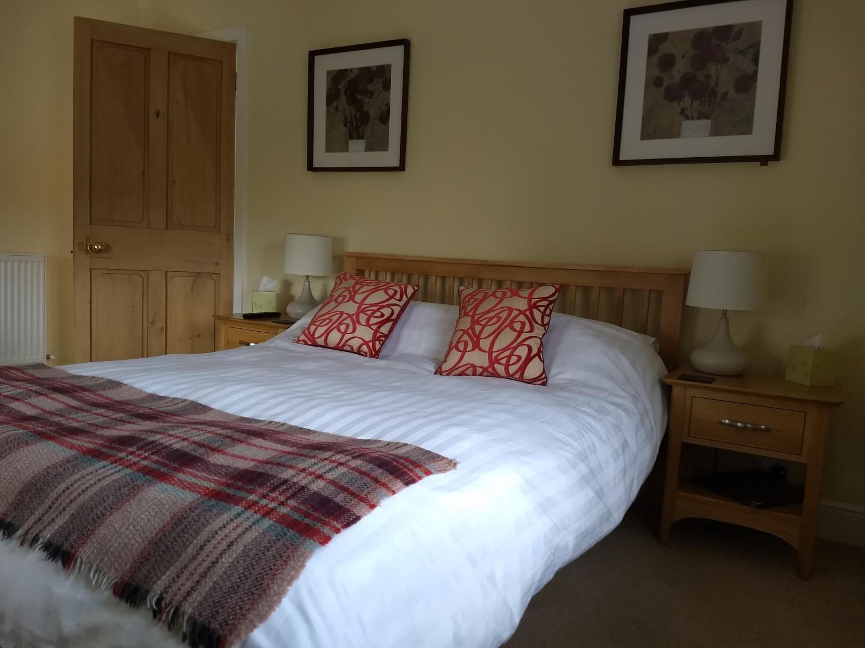 A bedroom with a bed, two bedside tables, a wooden wardrobe, and two framed pictures on the wall.