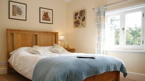 A bedroom with a wooden bed, a blue blanket, and a window with curtains.
