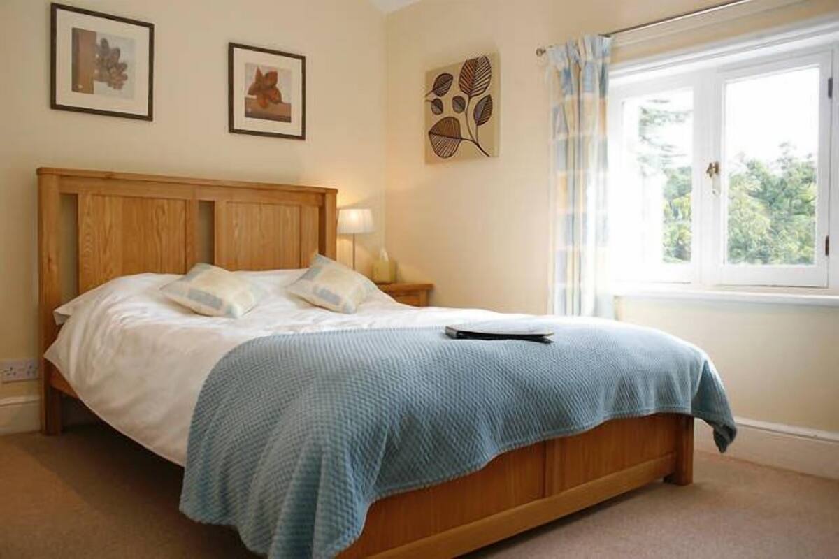A bedroom with a wooden bed, a blue blanket, and a window with curtains.